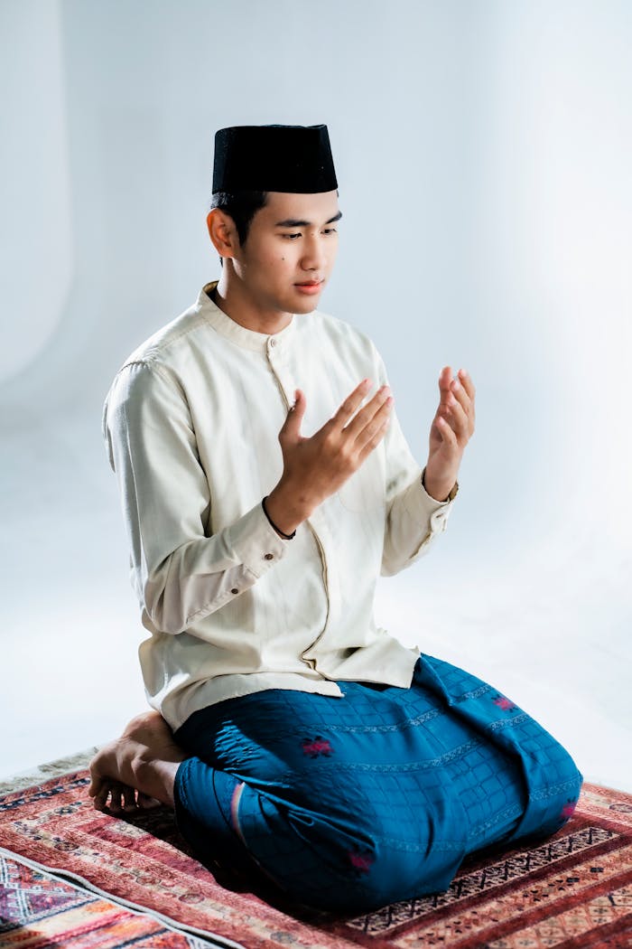 A young man in traditional attire praying indoors, showcasing cultural heritage.